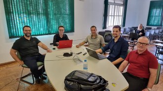 Cinco homens, sentados ao redor de mesa oval