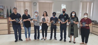 Oito pessoas posam para a foto segurando um livro na mão