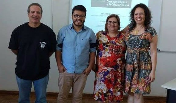 Quatro pessoas, uma ao lado da outra, em uma sala de aula olhando para a câmera.