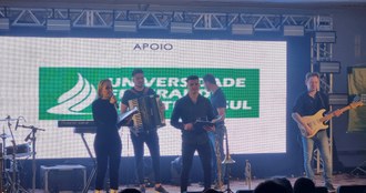 Integrantes da Banda Indústria Musical em apresentação, na tela ao fundo a logomarca da UFFS