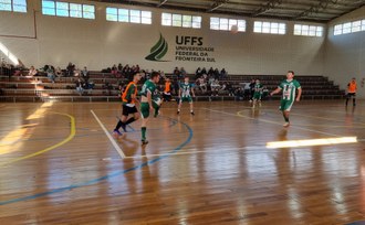 Jogo de futsal, ao fundo a arquibancada e a logomarca da UFFS