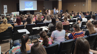Imagem do auditório do bloco C, com muitas pessoas sentadas, de costas, e, ao fundo, quatro pessoas estão à frente, falando aos participantes