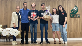 Foto de três mulheres e três homens, em cima de um palco, com a marca da UFFS atrás, na parede. Dois homens estão com premiações nas mãos