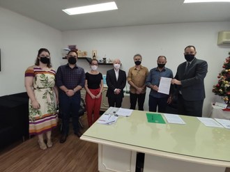 Em uma sala estão as autoridades (Coordenadora Acadêmica da UFFS - Campus Chapecó, Gabriela Gonçalves de Oliveira, o médico e articulador do protocolo, Diego Corso, Secretária de Saúde de Xanxerê, Francis Mara Zago Pegoraro, Diretor da UFFS - Campus Chapecó, Roberto Mauro Dall'Agnol, prefeito eleito de Xanxerê, Oscar Martarello, prefeito de Xanxerê em exercício, Avelino Menegolla, Reitor da UFFS, Marcelo Recktenvald), em pé. O Reitor e o prefeito seguram o documento.