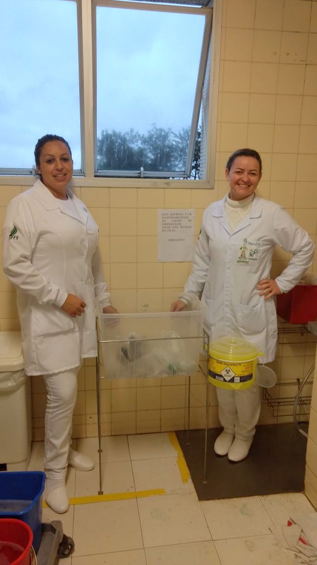 Cada uma das estudantes está de um lado do suporte com a caixa, projeto idealizado por elas