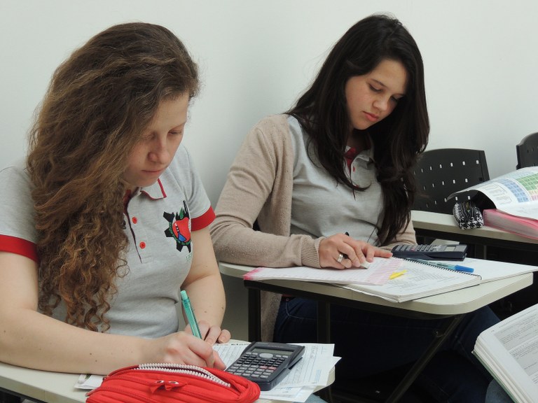 Duas meninas estudantes sentadas nas cadeiras em sala de aula realizando exercícios da disciplina 
