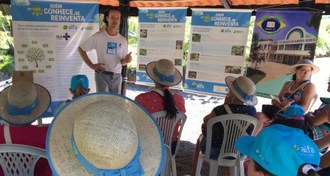Foto em plano médio com público sentado de costas e professor explanando, de frente