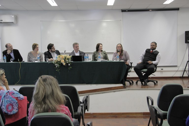 Parte do público está de costas e, de frente estão os componentes da mesa de honra