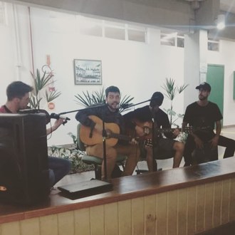 Quatro jovens sentados em cadeiras com microfones à frente e instrumentos musicais