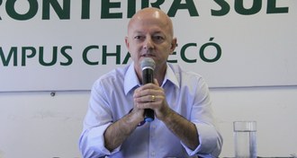 Professor aparece falando em um microfone, em frente a uma placa da UFFS - Campus Chapecó