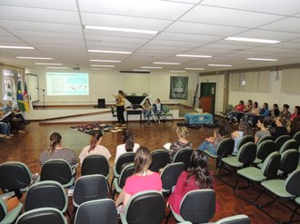 Professora de pé falando para público que está sentado