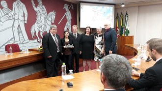 Professora com troféu na mão, de pé, com mais cinco pessoas ao redor