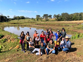 Foto mostra um grupo de pessoas posando para foto. Ao fundo vários tanques de cultivo de peixes.