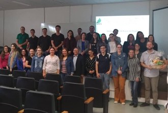 Na imagem várias os estudantes e professores do curso, em pé, posam para foto no auditório.