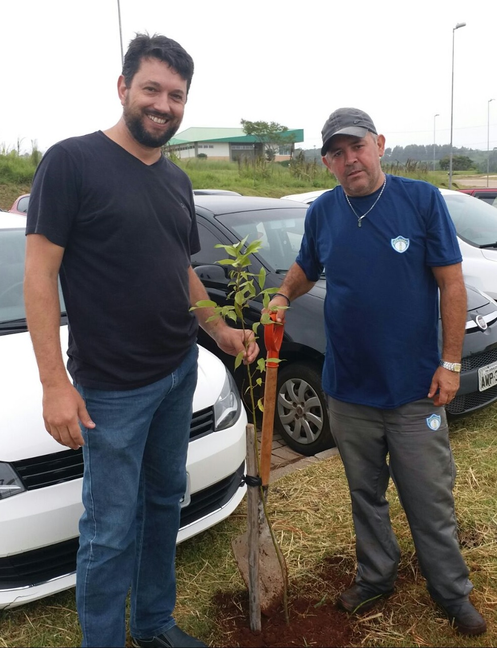 Na foto dois homens posam com a primeira muda plantada pelo projeto.