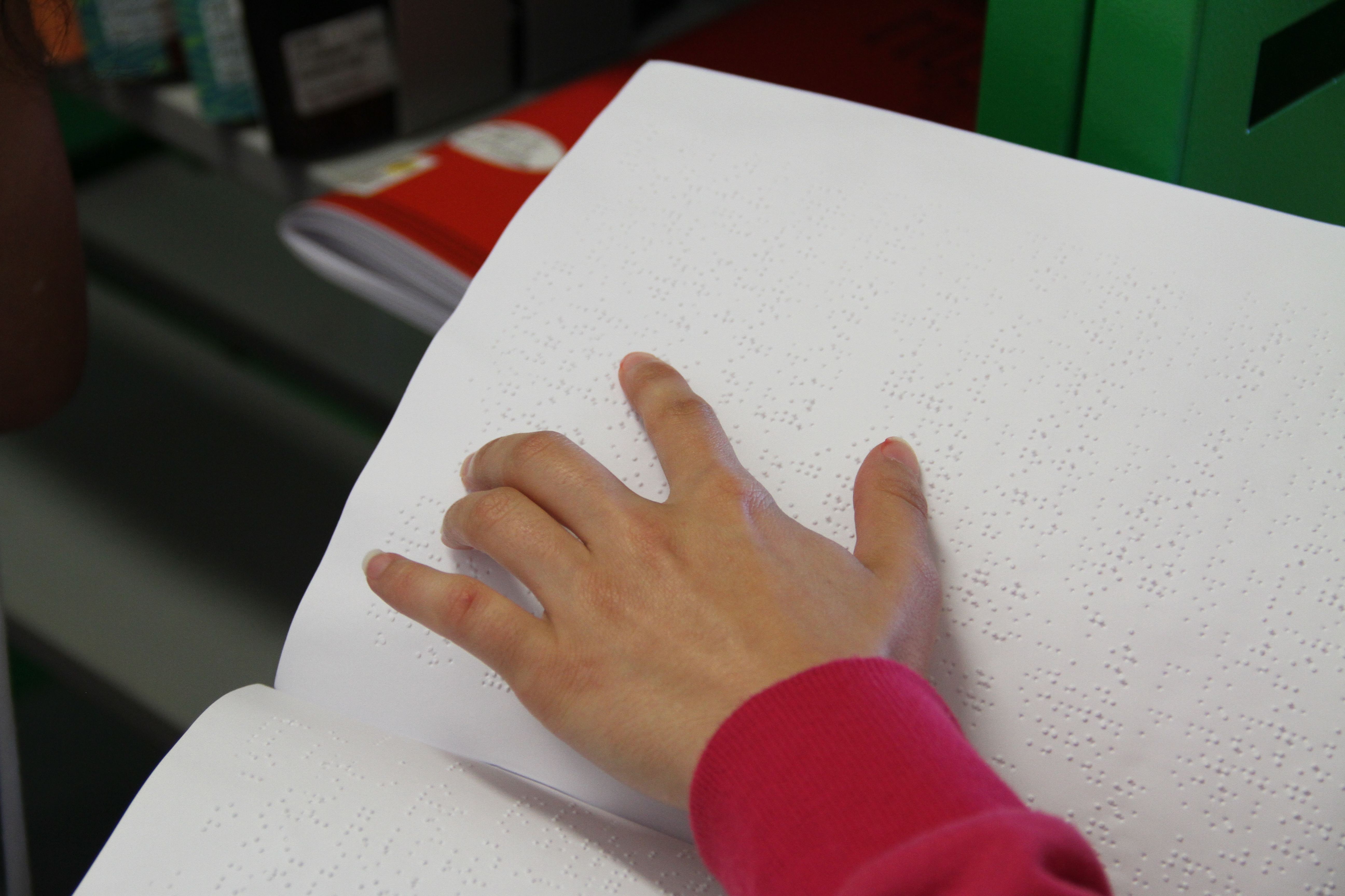 Foto em plano fechado de uma mão sobre um livro escrito em sistema braille.