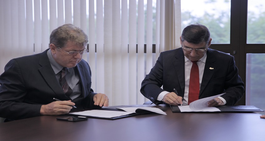 Foto focando os dois reitores sentados à mesa assinando os termos do contrato
