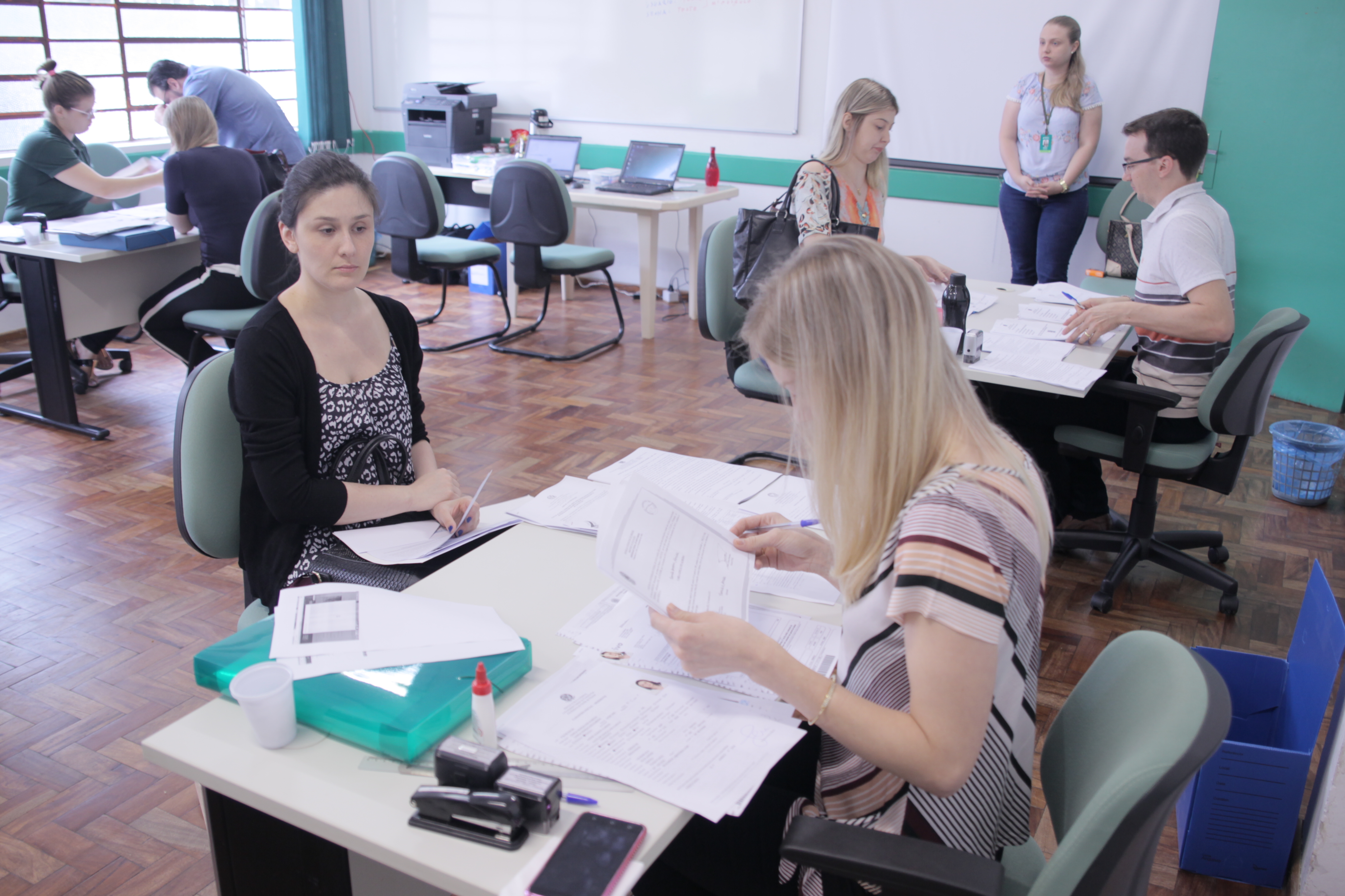 Foto em plano aberto mostrando diversas pessoas sendo atendidas sentadas ao fundo, centralizando uma dupla de atendente e servidor da UFFS