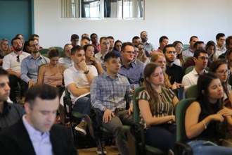 Foto em plano aberto, do auditório, onde os residentes estão sentados, de frente, observando o auditório