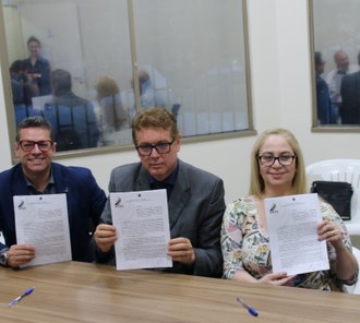 Foto em plano médio destacando os participantes sentados lado a lado e mostrando o termo do convênio