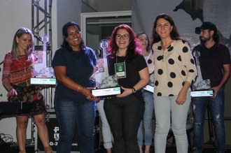 Três mulheres, duas delas seguram um troféu.