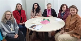 seis mulheres sentadas ao redor de uma mesa olham para a foto sorrindo