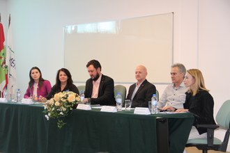 Na foto aparece uma mesa com três mulheres e três homens sentados atrás dela