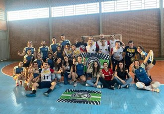 estudantes posam para foto. vários homens e mulheres em pé e também sentados. Na frente deles no chão uma bandeira estendida.