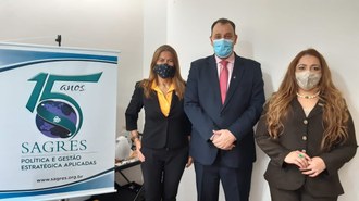 uma mulher, um homem e outra mulher posam de pé para a foto. No lado esquerdo há um banner onde se lê: 15 anos Sagres política e gestão estratégica aplicada