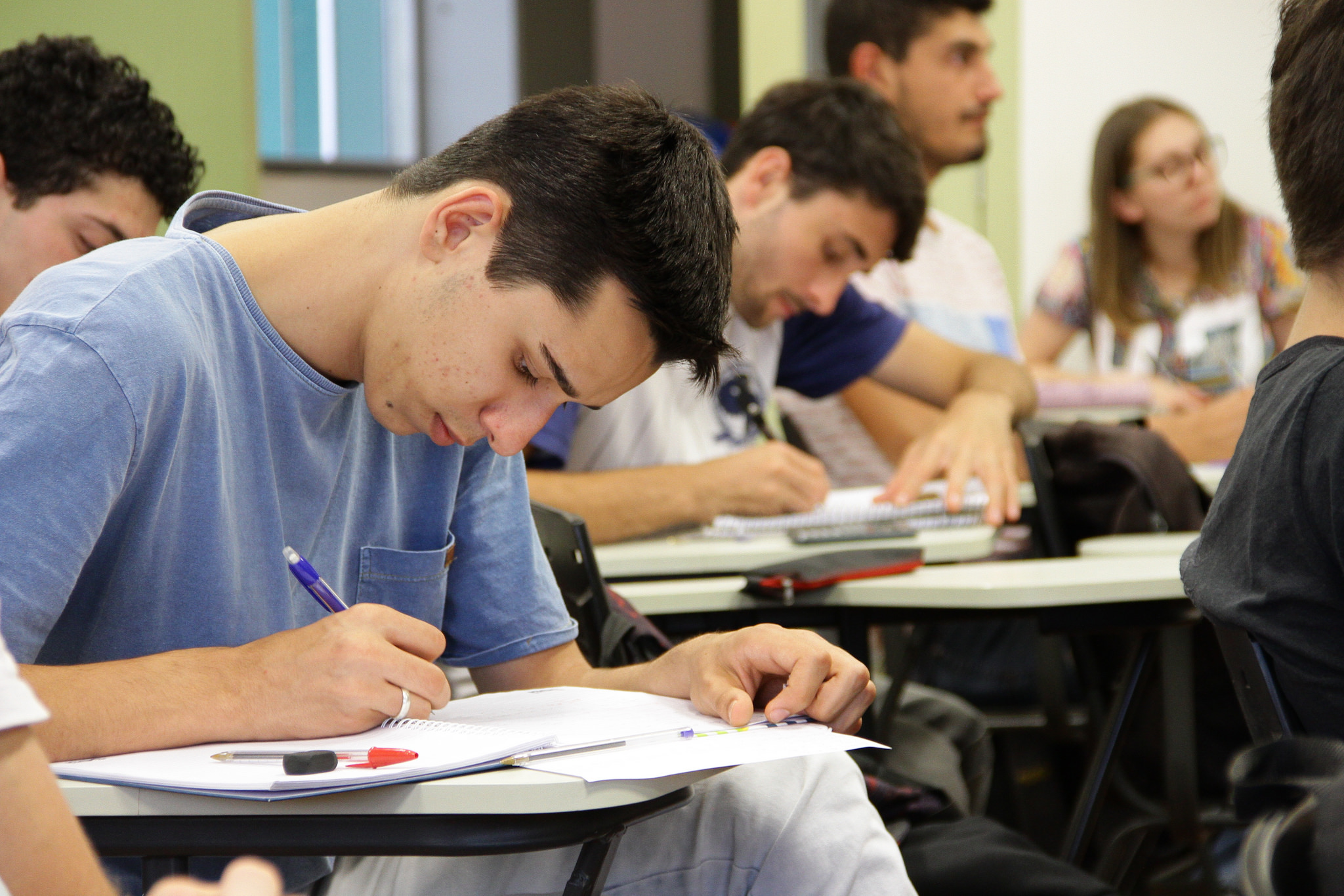 Aluno sentado em uma carteira escolar escreve em um caderno